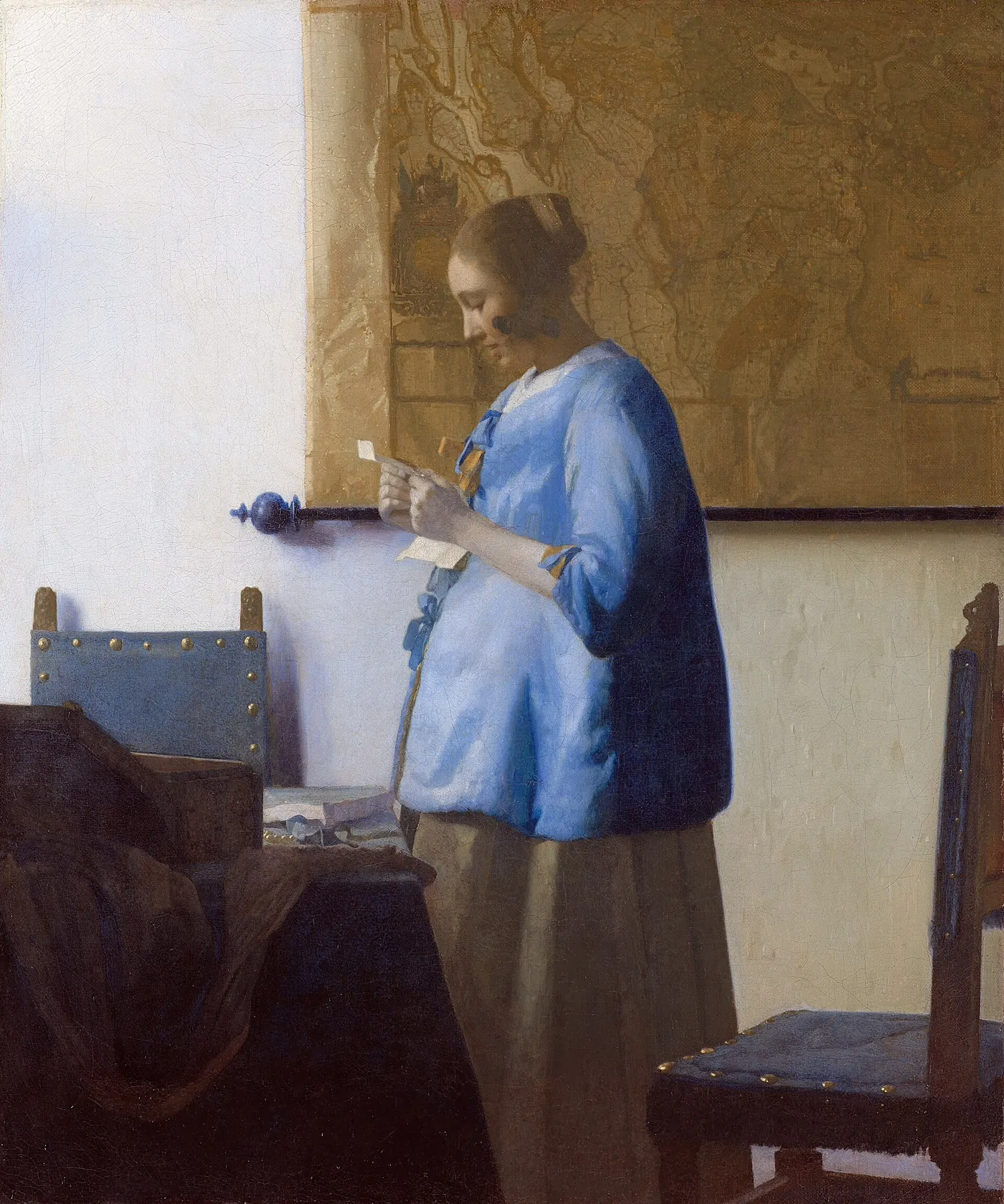 Johannes Vermeer, Woman in Blue Reading a Letter: a woman stands by a map, reading a letter held in both hands.